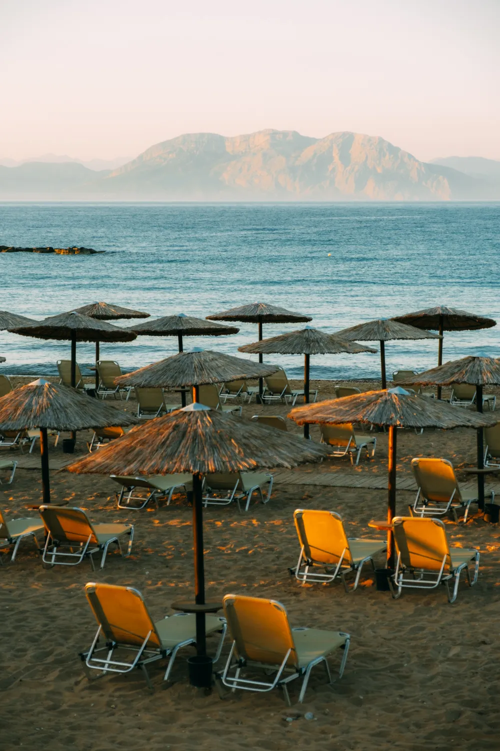 Rieten parasols en oranje ligbedden op het strand, bergen aan de horizon