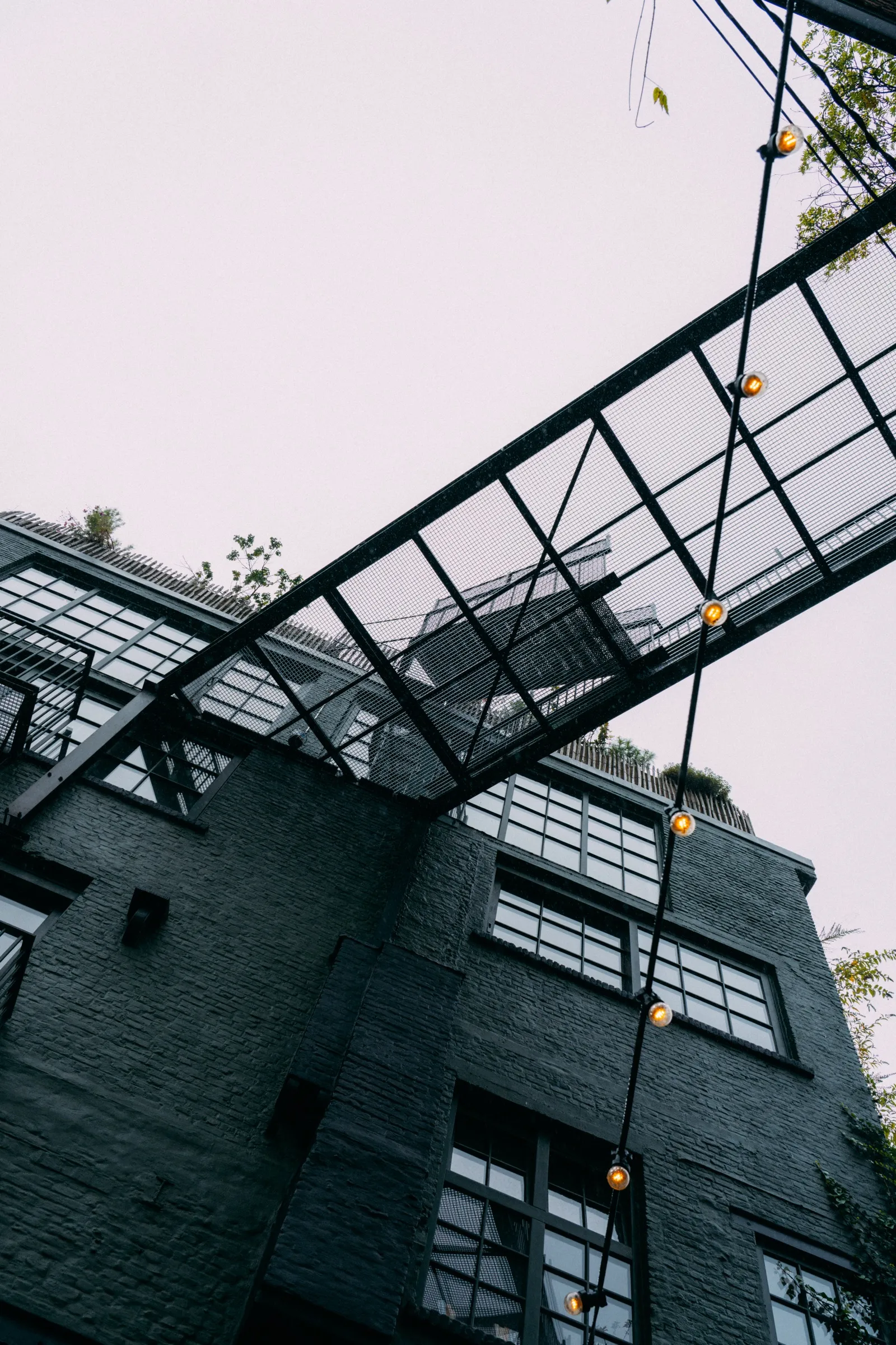 Zwart geschilderde gevel met een stalen loopbrug en lampenslinger